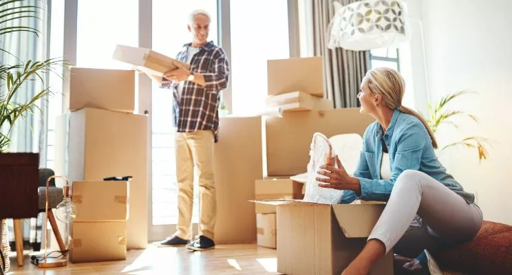 Older couple unpacking moving boxes in a sunny new home