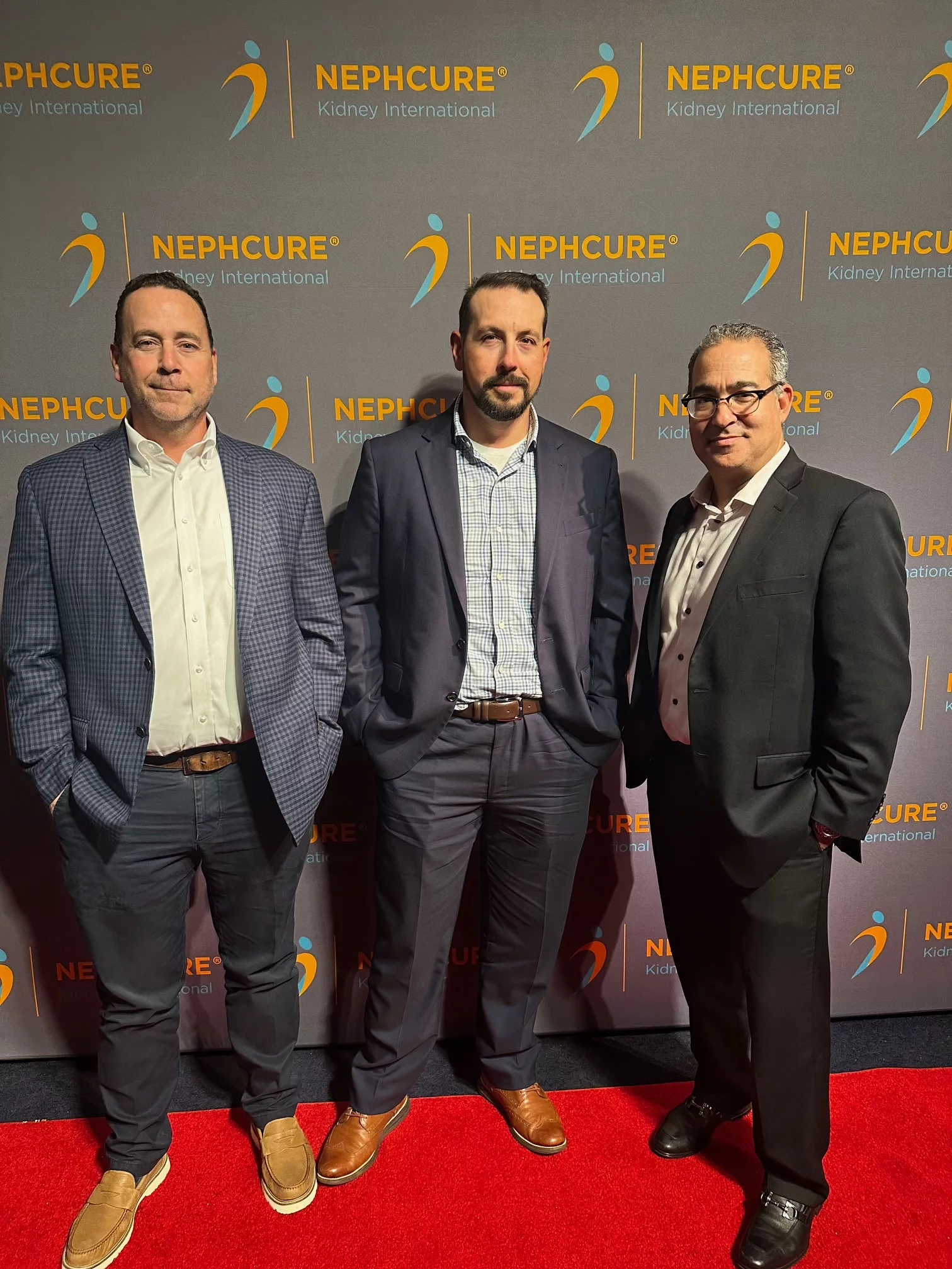 Three men in suits on the red carpet in front of a NephCure backdrop