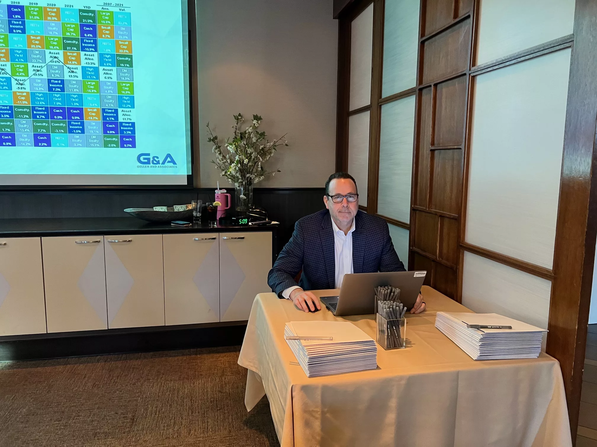 Advisor seated at a registration table with a laptop and handouts, a chart projected behind him