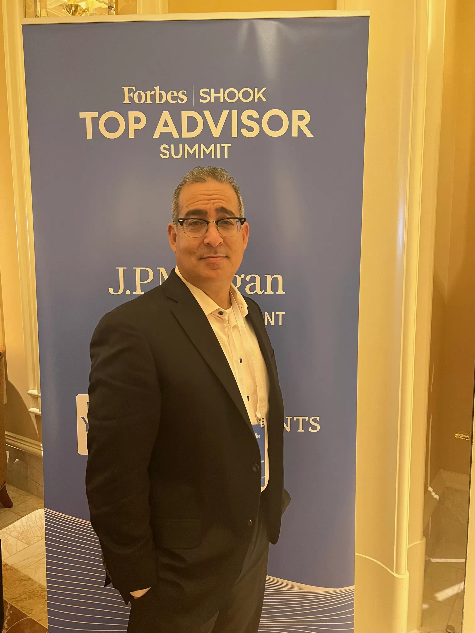 Advisor in a dark suit in front of a Forbes SHOOK Top Advisor Summit banner