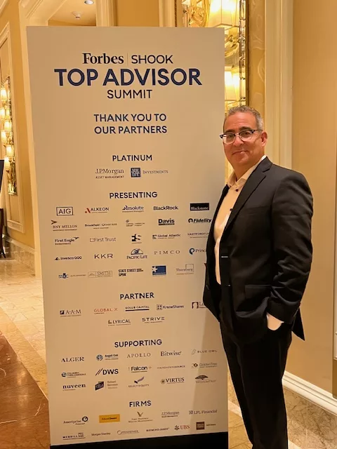 Advisor beside the Forbes SHOOK Top Advisor Summit sponsor banner