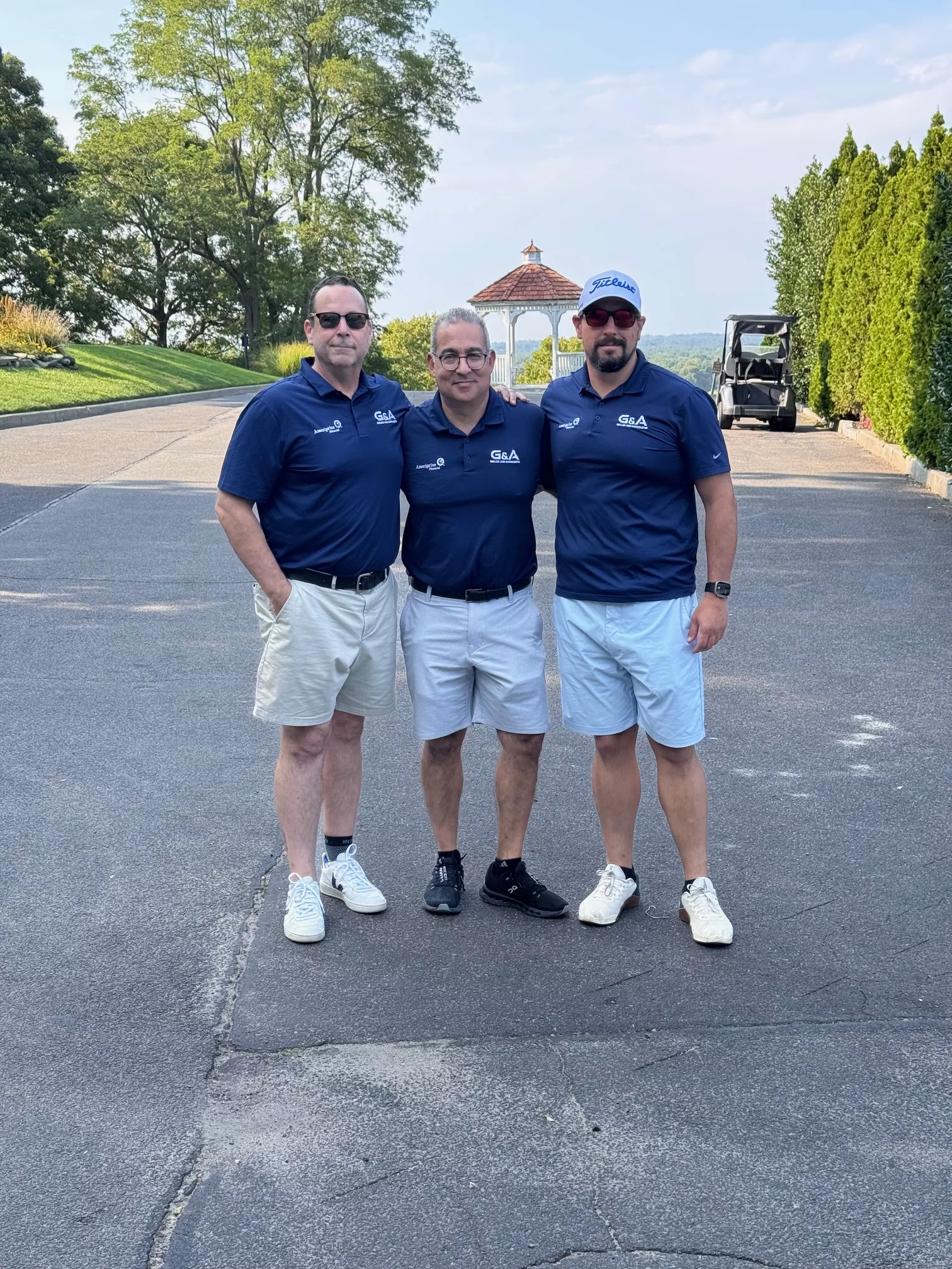 Three men in matching navy polo shirts and shorts on a golf course drive