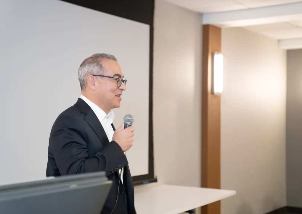 Advisor in a dark blazer speaking into a microphone in front of a projection screen