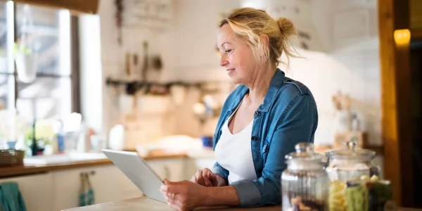 Woman in a denim shirt reading a tablet at her kitchen counter