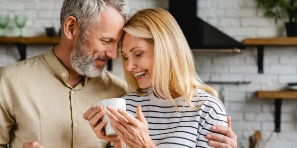 Smiling older couple embracing in a kitchen, the woman holding a white mug