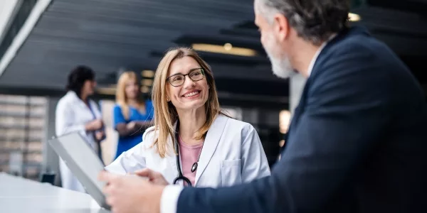 Smiling doctor in a white coat reviewing a tablet with a man in a suit