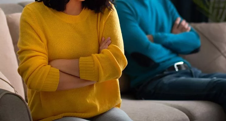 Couple sitting apart on a sofa with arms crossed