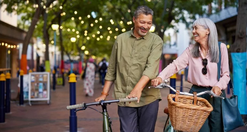 Older couple walking bikes down a tree-lined street with string lights