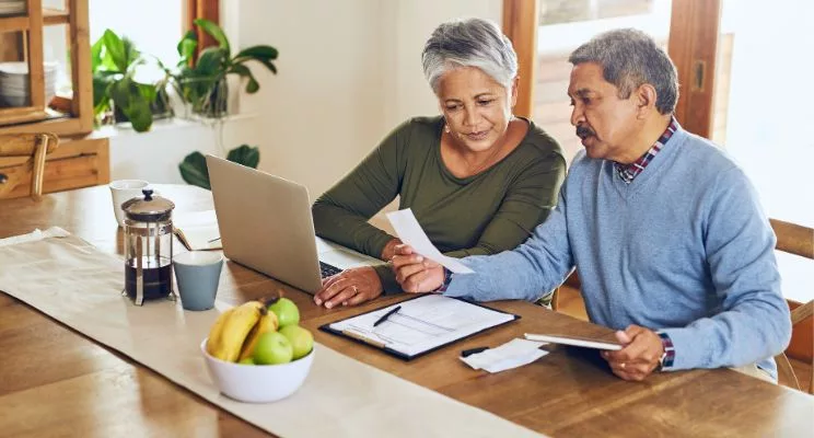 Older couple at the kitchen table reviewing tax papers on a laptop