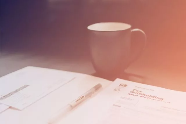 Tax withholding forms and a pen on a desk beside a coffee mug
