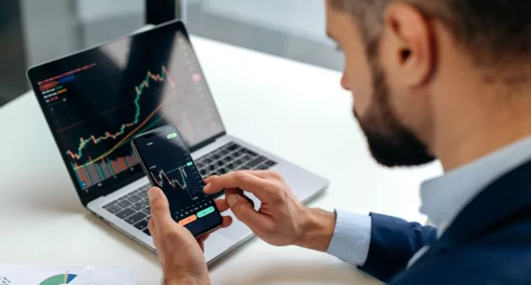 Investor checking a stock chart on his phone in front of a laptop
